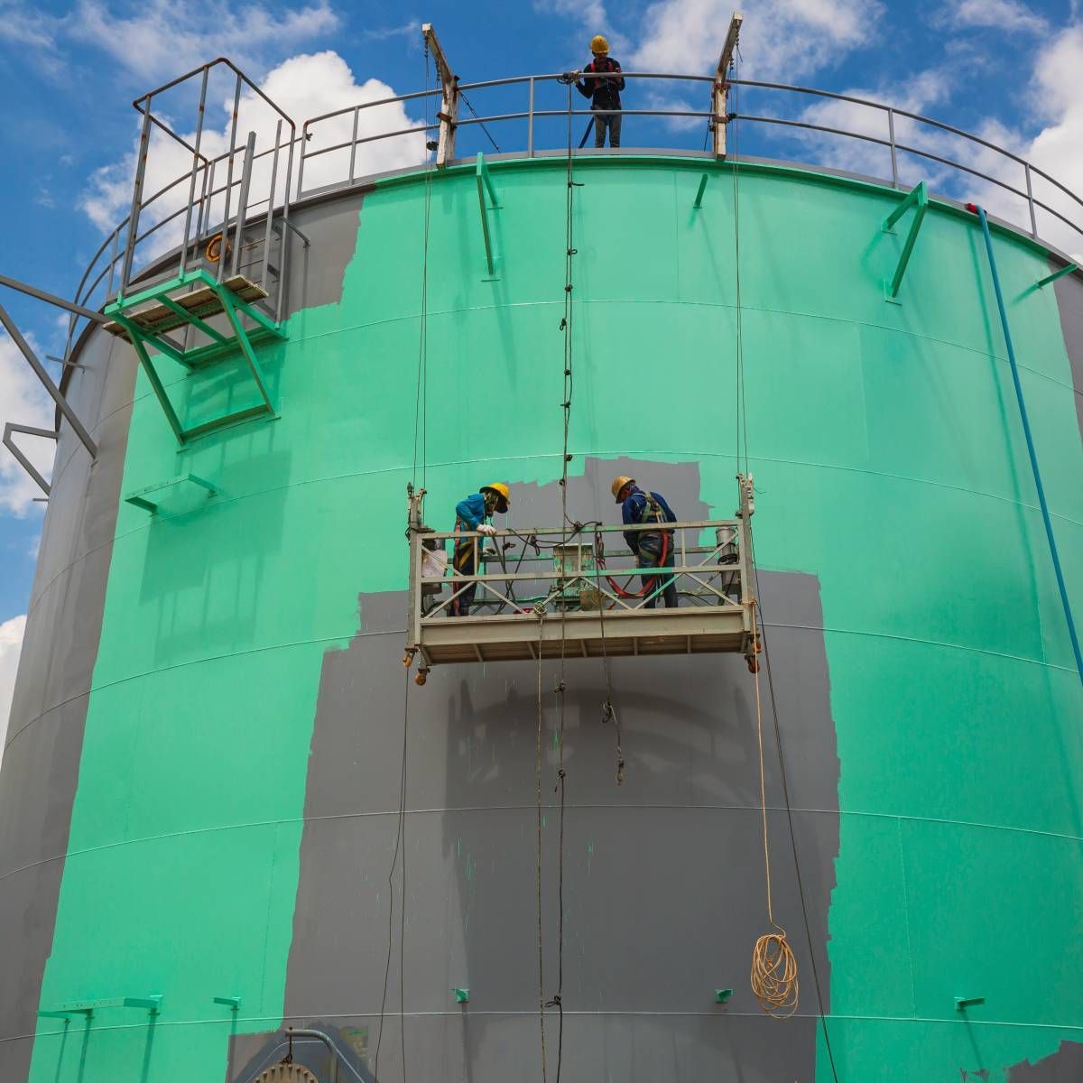 Two men are painting a large building with green paint