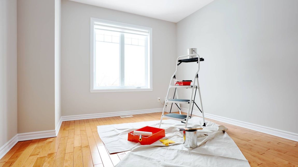 An empty room with a ladder and paint supplies on the floor.