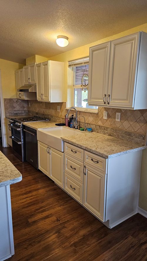 A kitchen with white cabinets, granite countertops, a farmhouse sink, and dark wood floors.