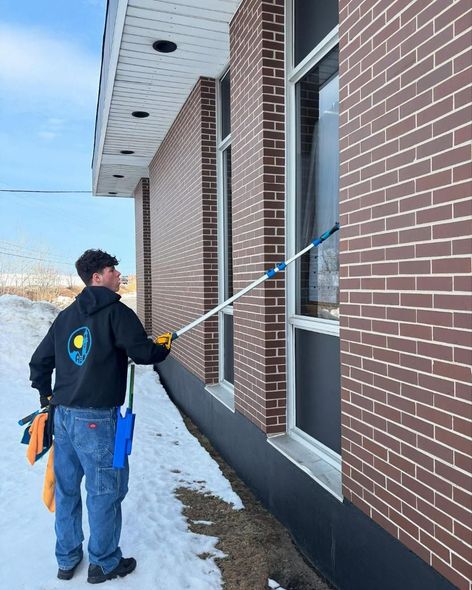 A man is cleaning a window on the side of a brick building.