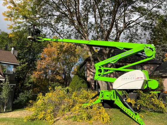 A green crane is used cutting a tree in front of a house.