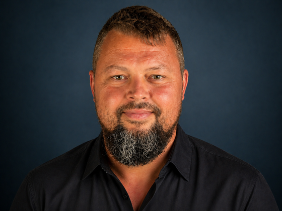 Man in gray shirt with beard sitting in a car, smiling. On Time Tree logo on shirt.