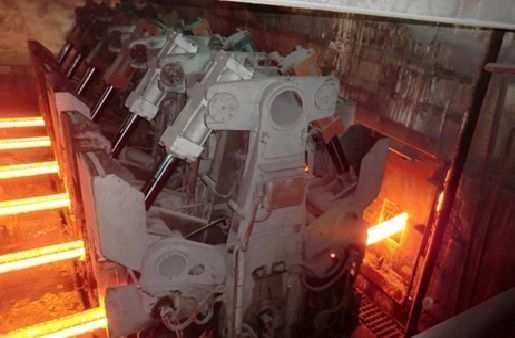 Hot steel bar rolling through industrial machinery.