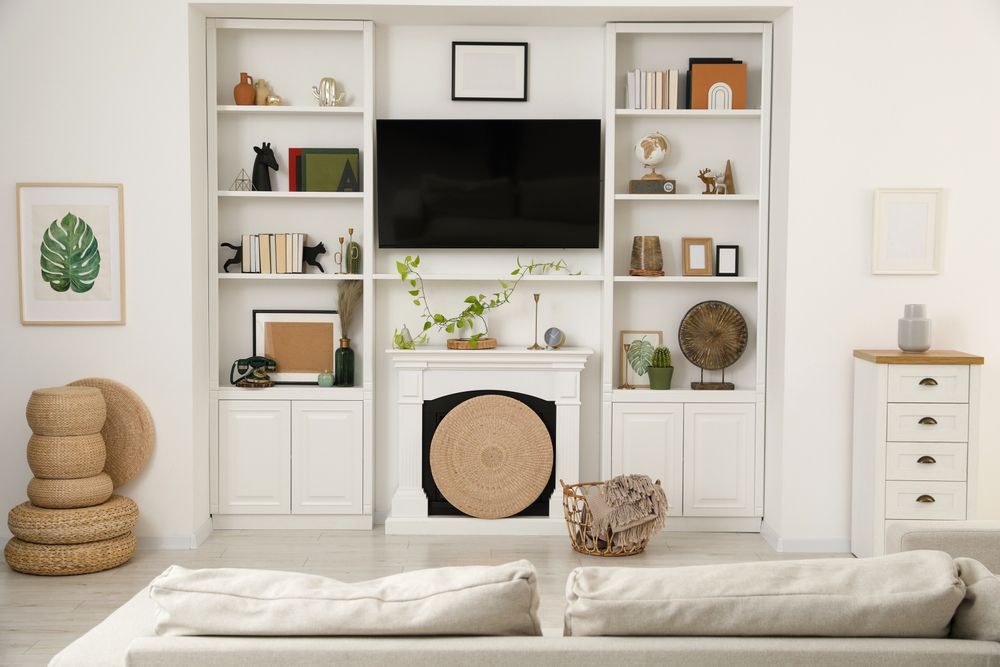 A living room with a couch , fireplace , shelves and a flat screen tv.
