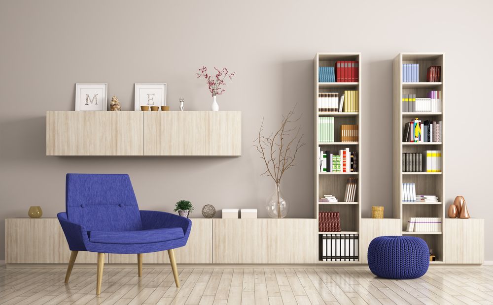 A living room with a blue chair , bookshelves , and ottomans.