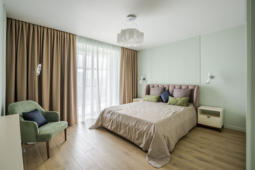 A bedroom with a bed , chair , nightstand and curtains.
