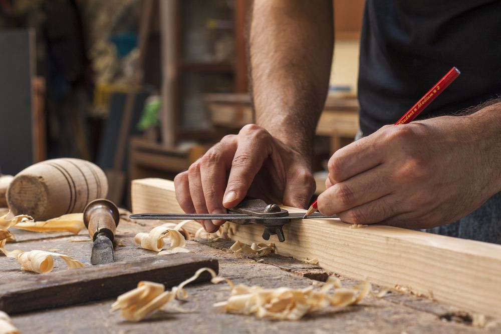 A man is measuring a piece of wood with a tape measure.