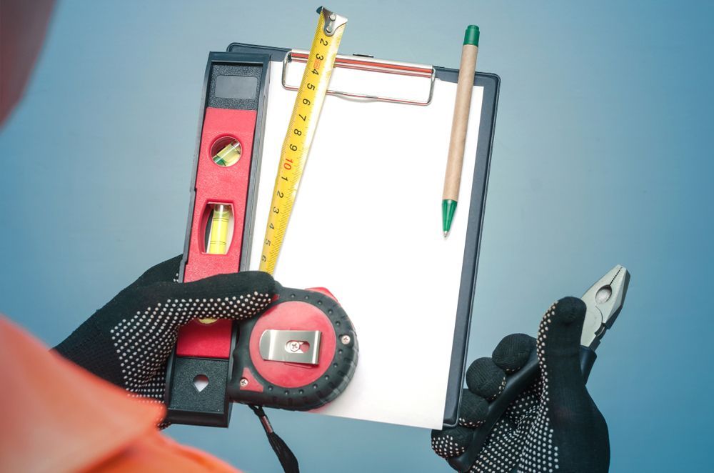 A person is holding a clipboard with a tape measure , level and pencil on it.