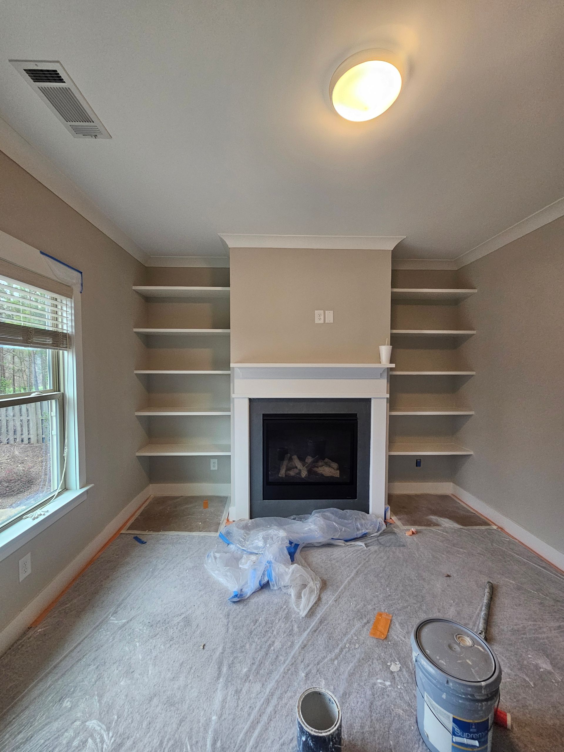 A living room with a fireplace and shelves is being painted.