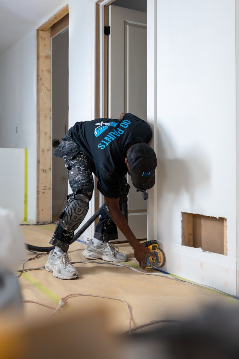 Person sanding a wooden floor next to a white wall and doorway. Construction site.