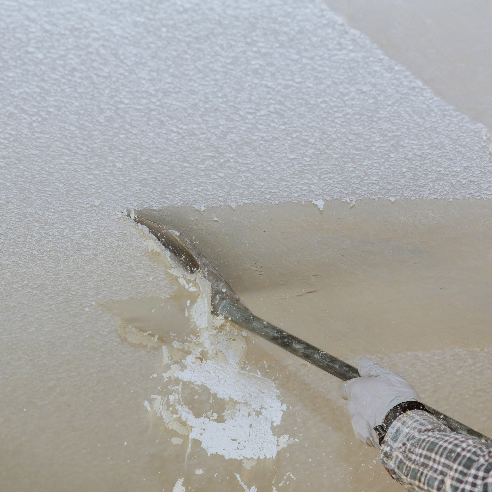 Person scraping a wet, light-colored surface with a metal tool; close-up view.