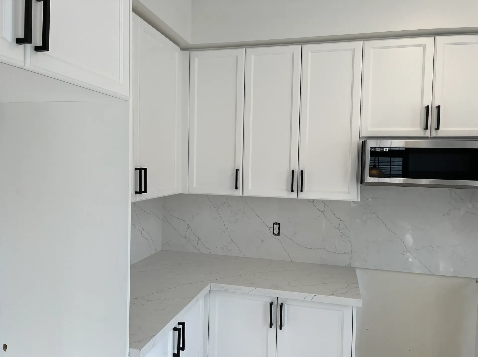 White kitchen cabinets with black handles and a stainless steel microwave.