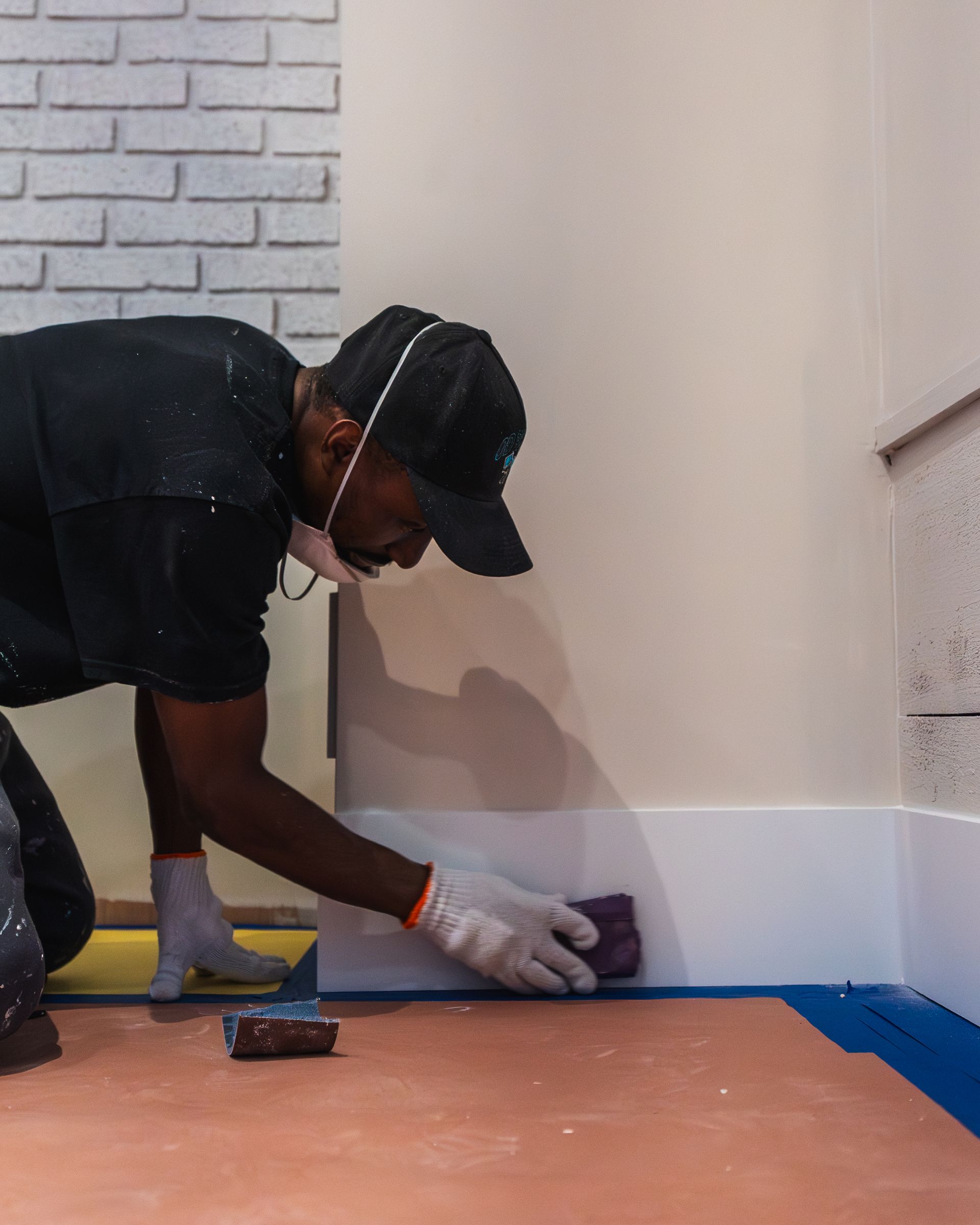 Person sanding baseboard trim near a white brick wall.