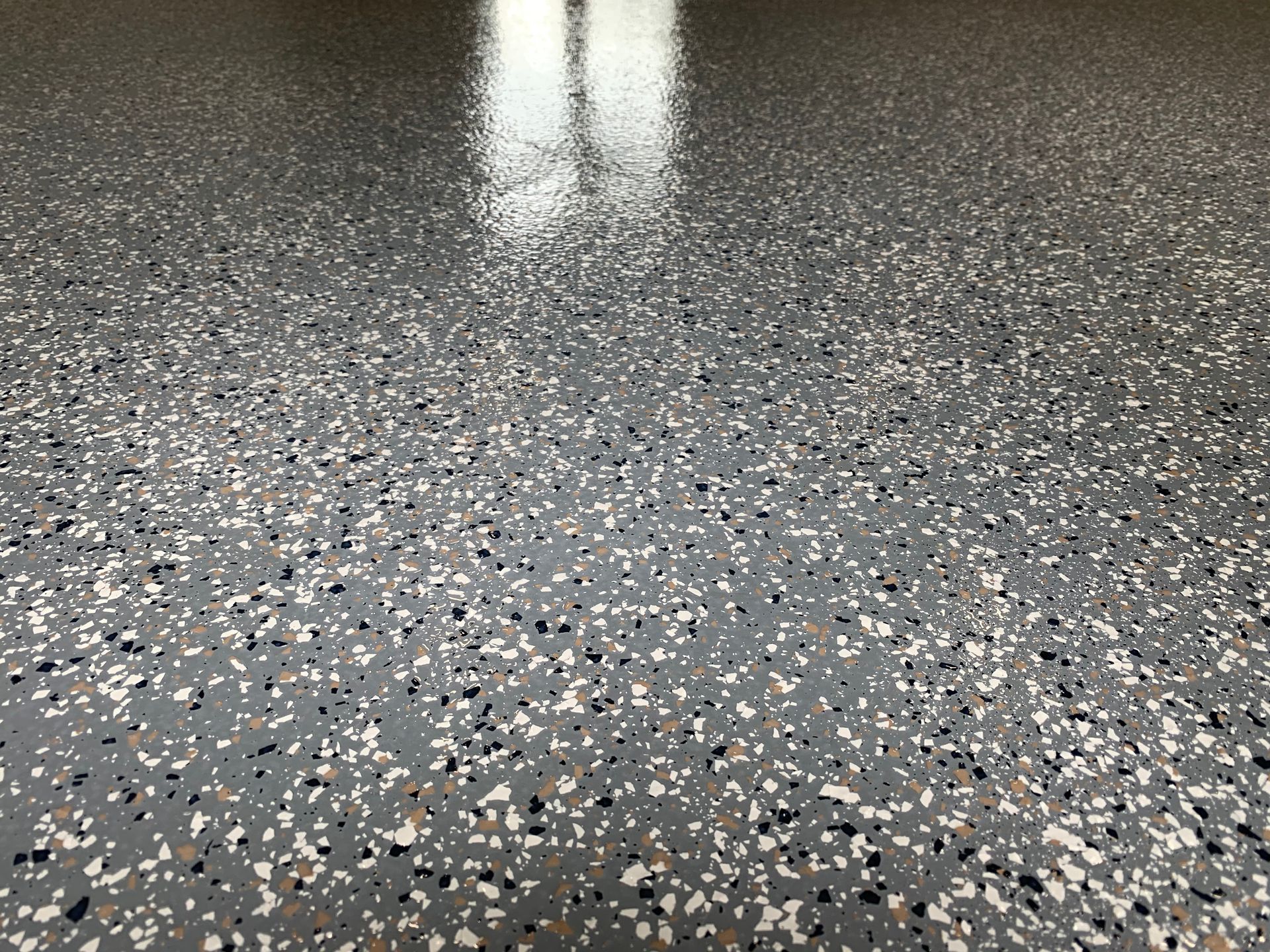 Plancher de garage en époxy avec des éclats gris mouchetés, noirs, blancs et beiges reflétant la lumière du plafond.