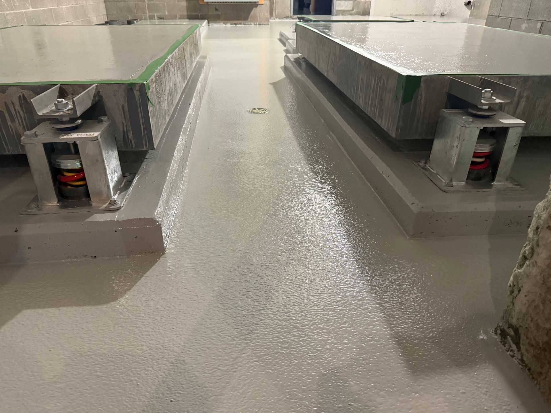 Deux grandes plateformes grises sur supports métalliques à ressorts rouges, sur un sol peint en gris.