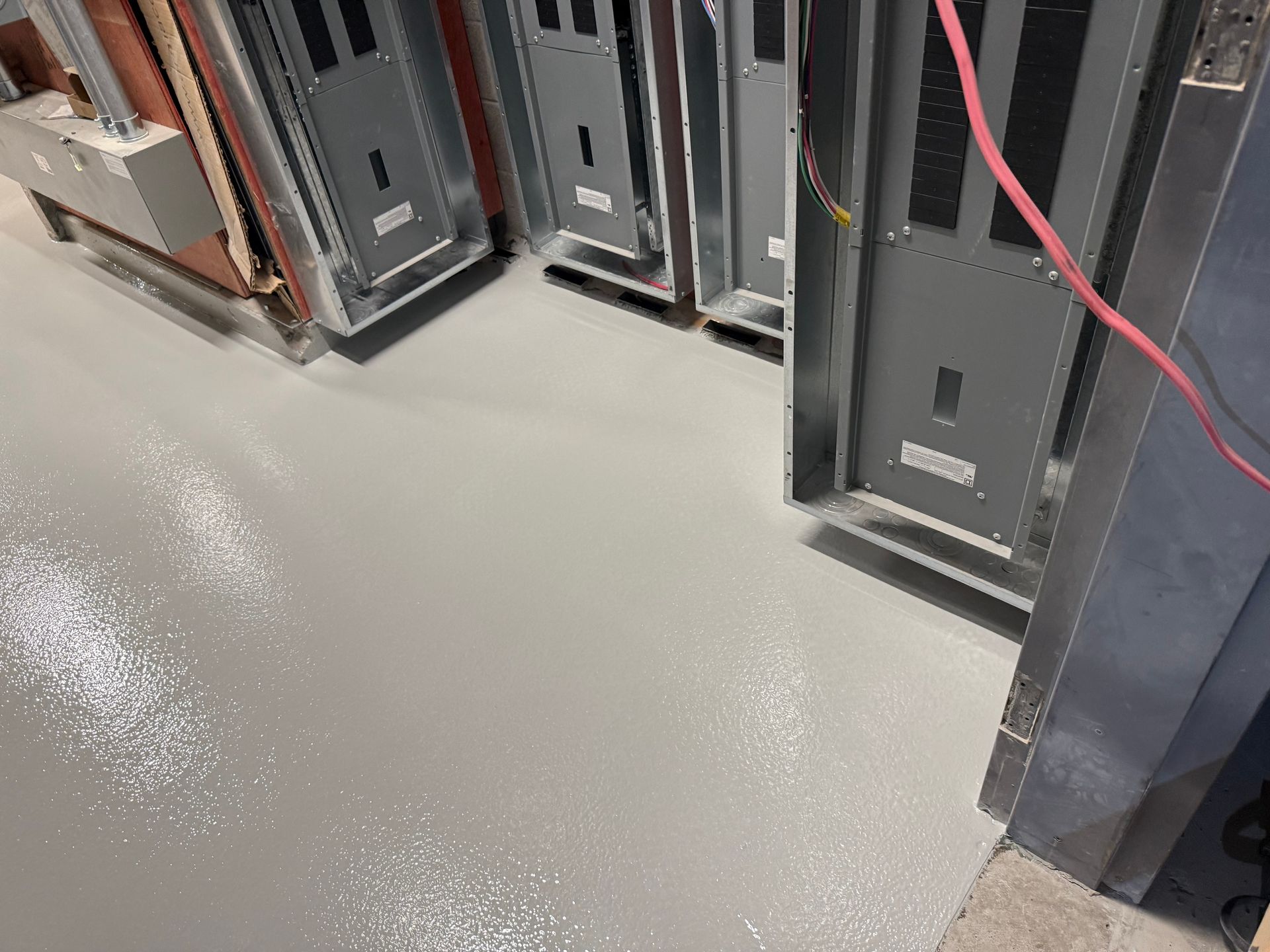 Plancher époxy gris clair dans une pièce avec panneaux électriques en métal.