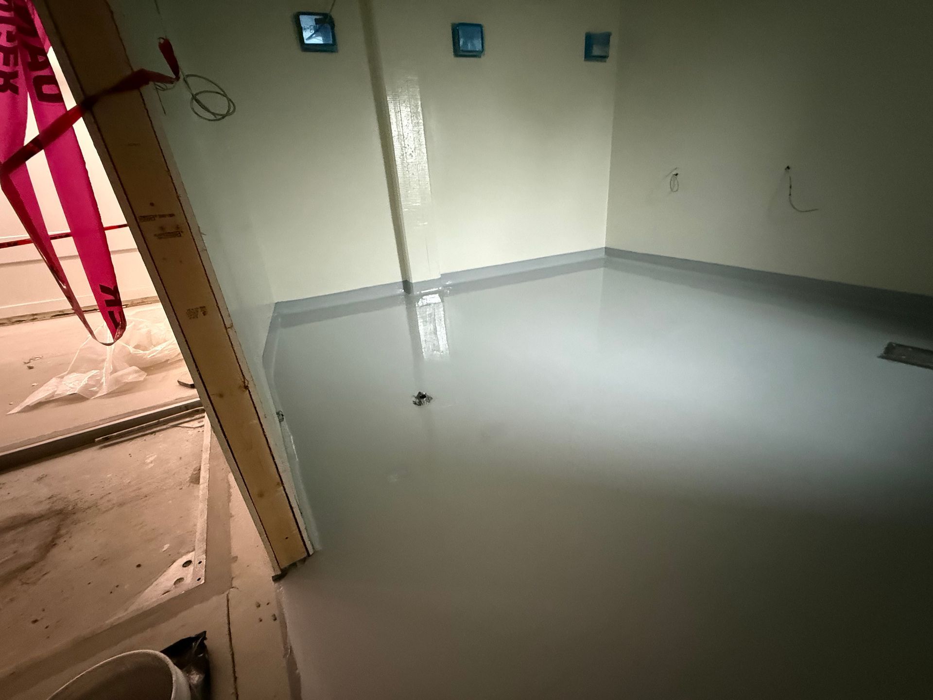 Sol époxy gris fraîchement coulé dans une pièce en construction; murs non finis, ruban de sécurité.