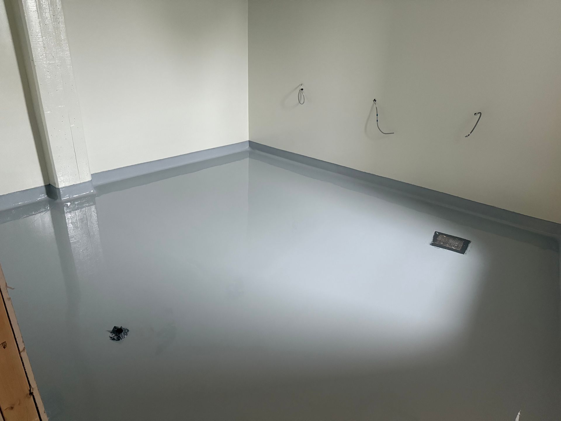 Sol époxy gris dans une petite pièce avec murs gris clair et conduites de plomberie.