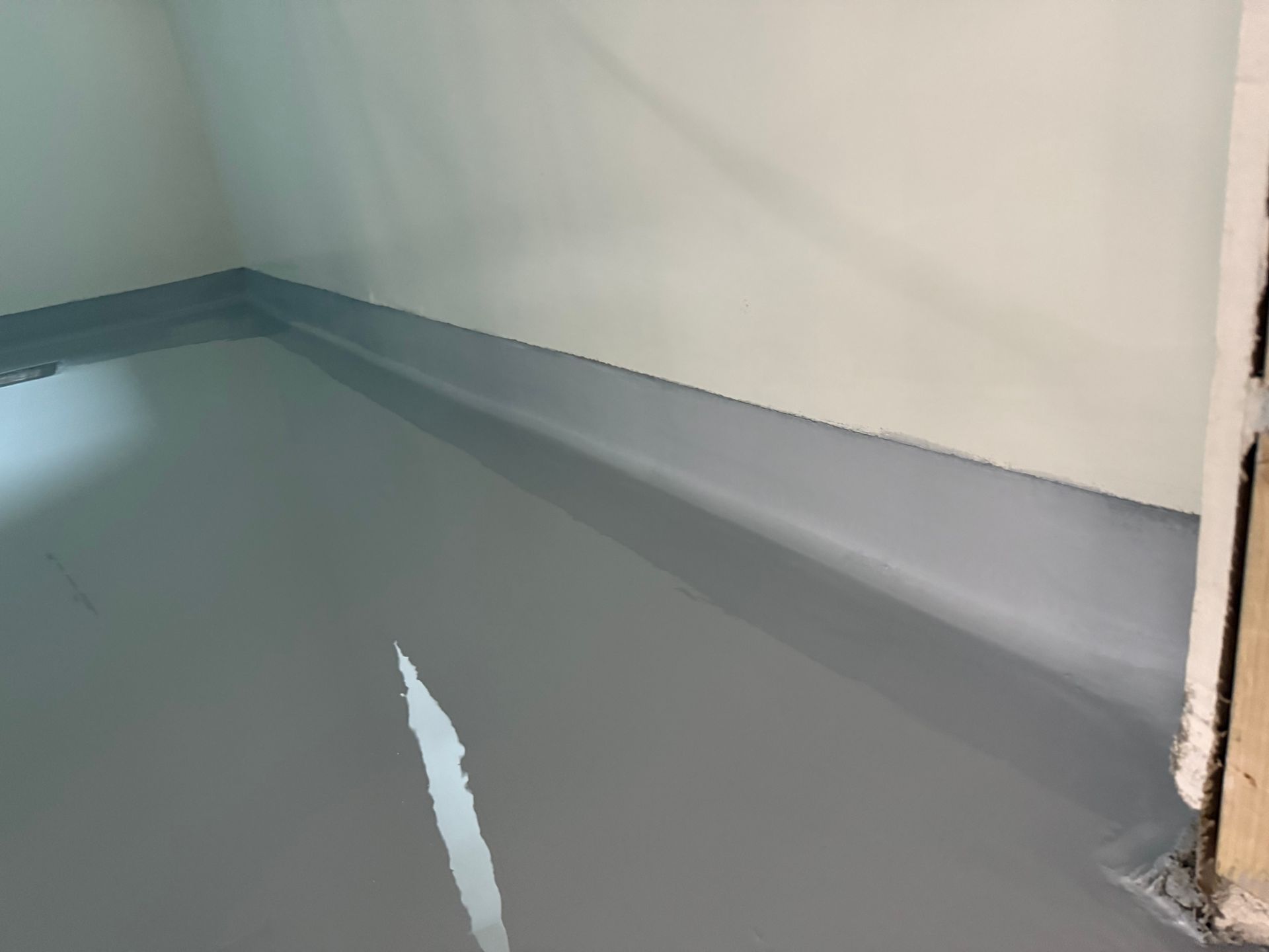 Plancher et plinthe en époxy gris dans une pièce aux murs blancs, porte partiellement visible.