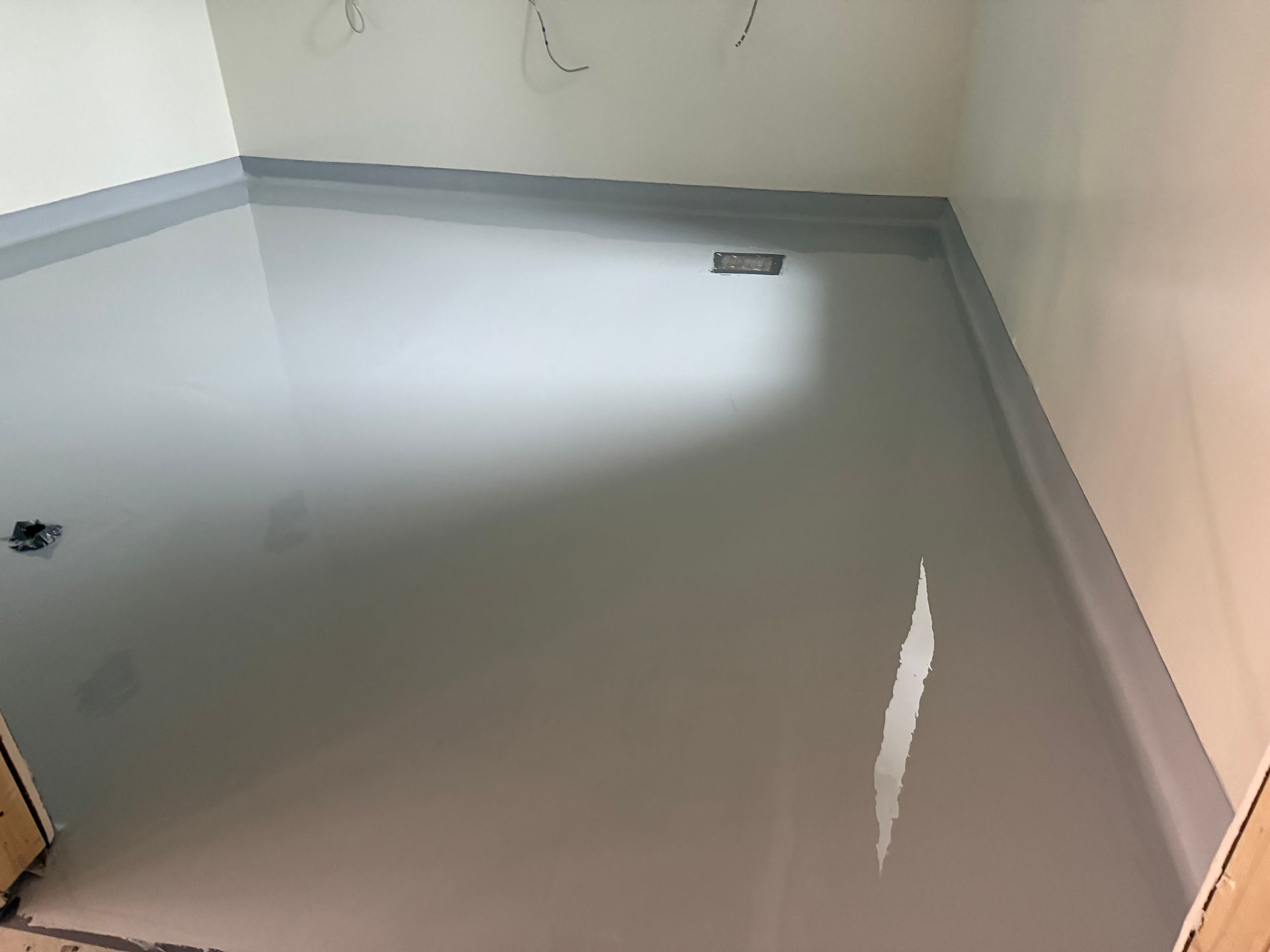 Plancher époxy gris dans une pièce, avec plinthes en alcôve et câblage visible sur les murs.