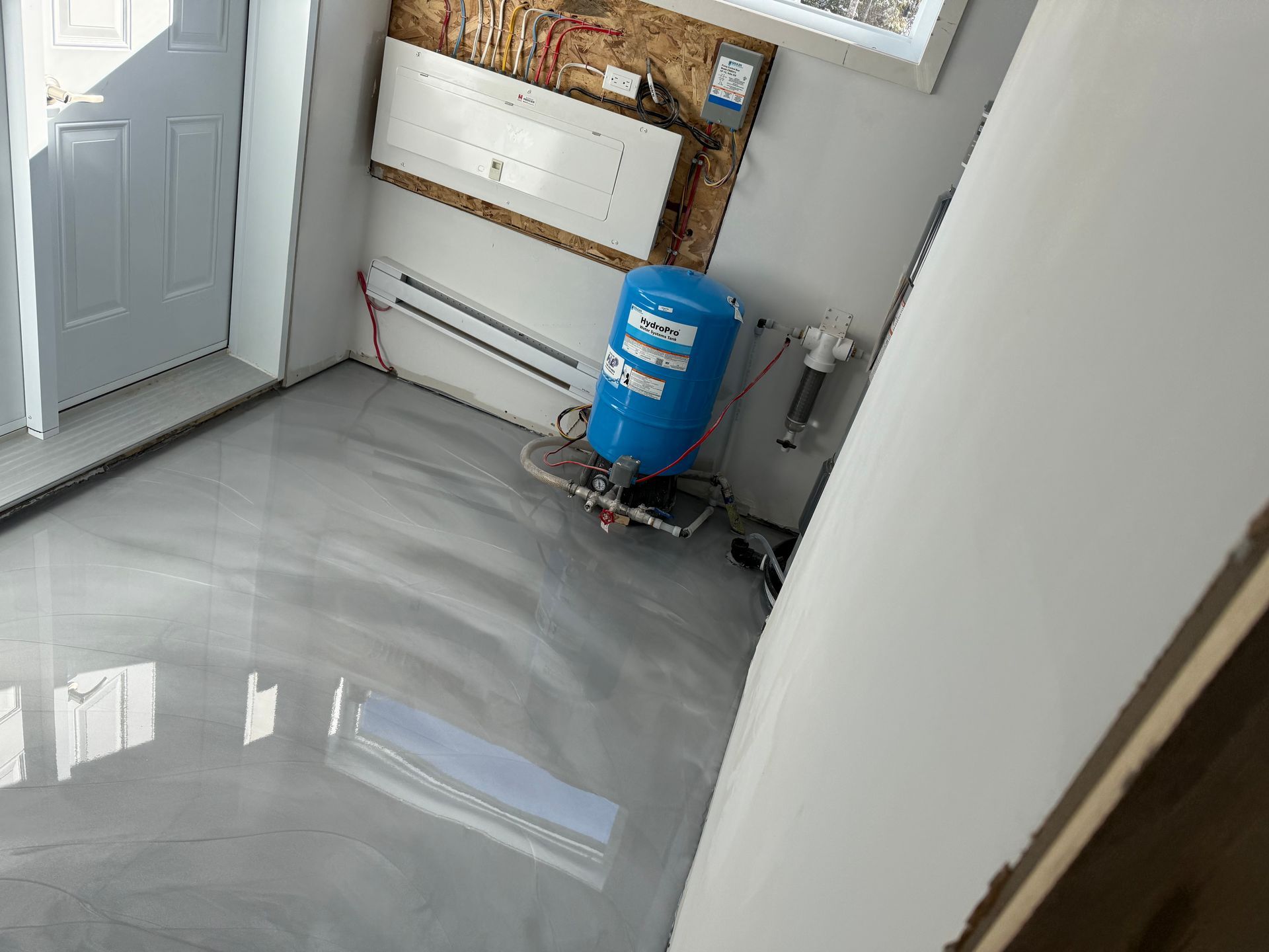 Intérieur de garage avec un sol époxy argenté brillant, réservoir d'eau bleu, porte blanche.