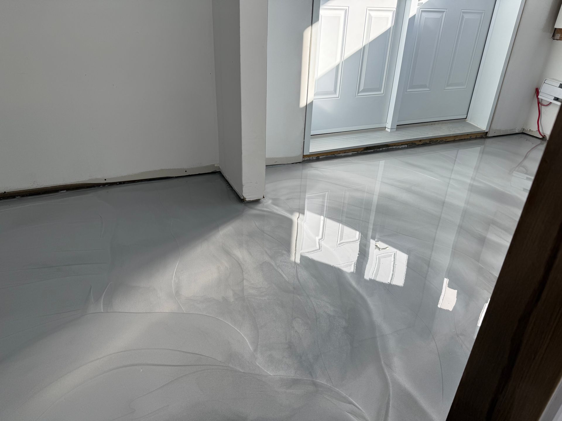 Sol époxy gris clair reflétant la lumière du soleil dans une pièce vide. Porte blanche en arrière-plan.