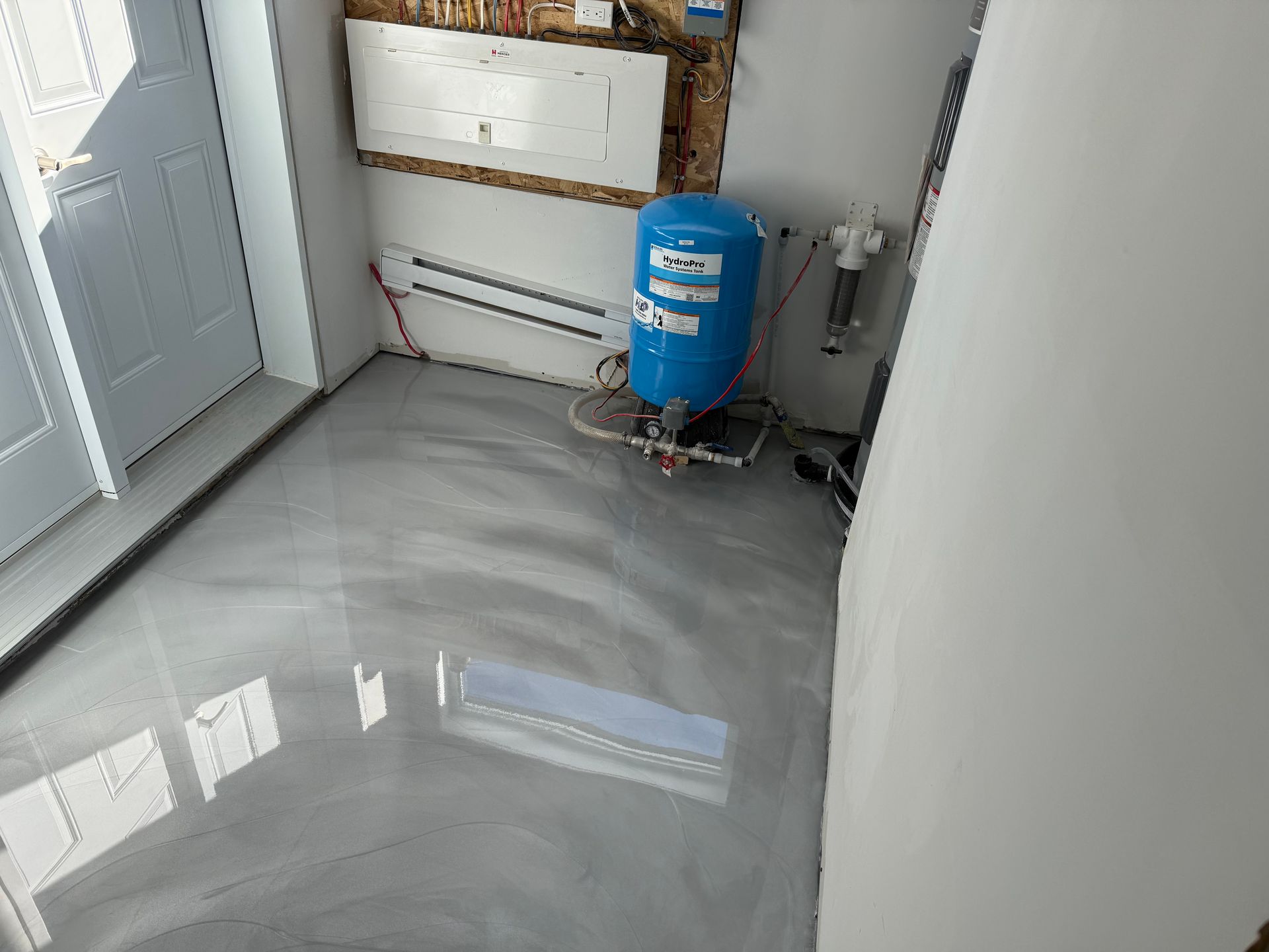 Une buanderie avec un sol gris métallique brillant, un réservoir d'eau bleu et une porte blanche.