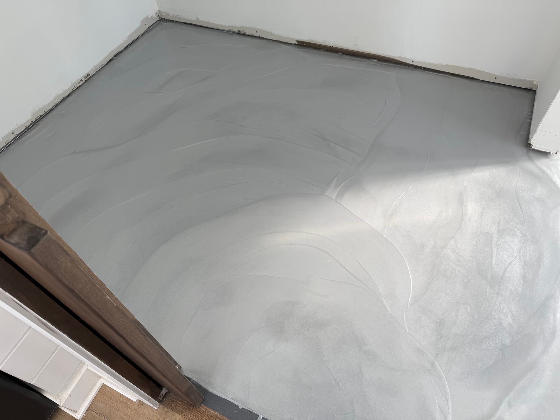 Sol en béton gris fraîchement coulé dans une pièce, avec des murs blancs et une porte visible.