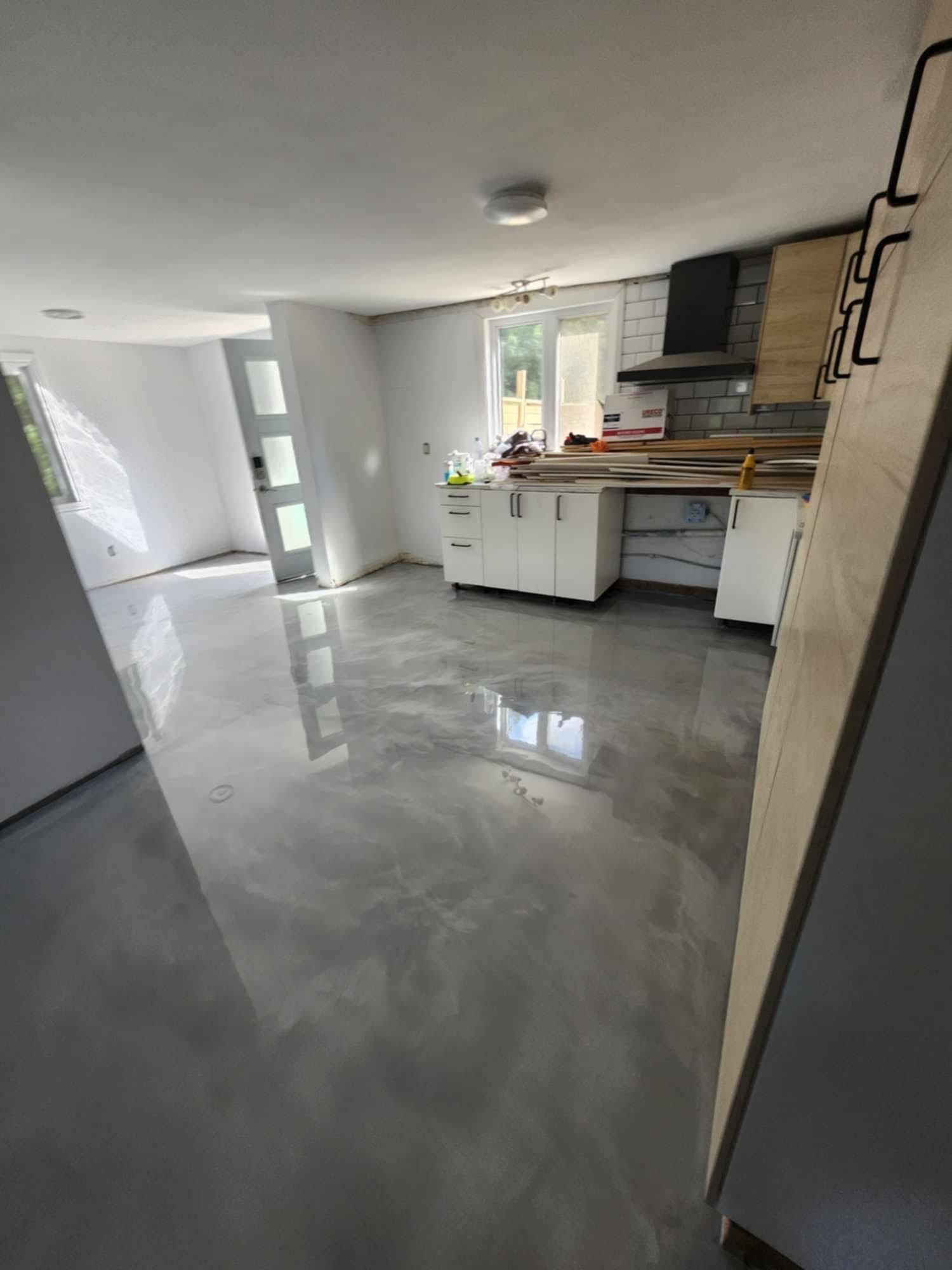 Cuisine vide avec sol en béton gris, armoires blanches et détails en bois brut.