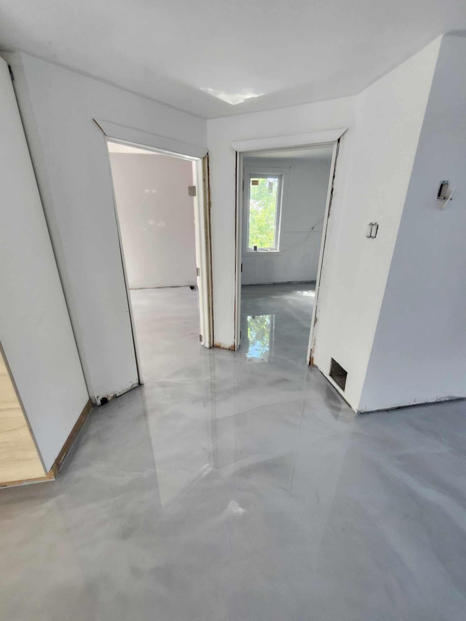 Sol époxy gris clair dans des pièces fraîchement peintes, avec des portes et une fenêtre visibles.