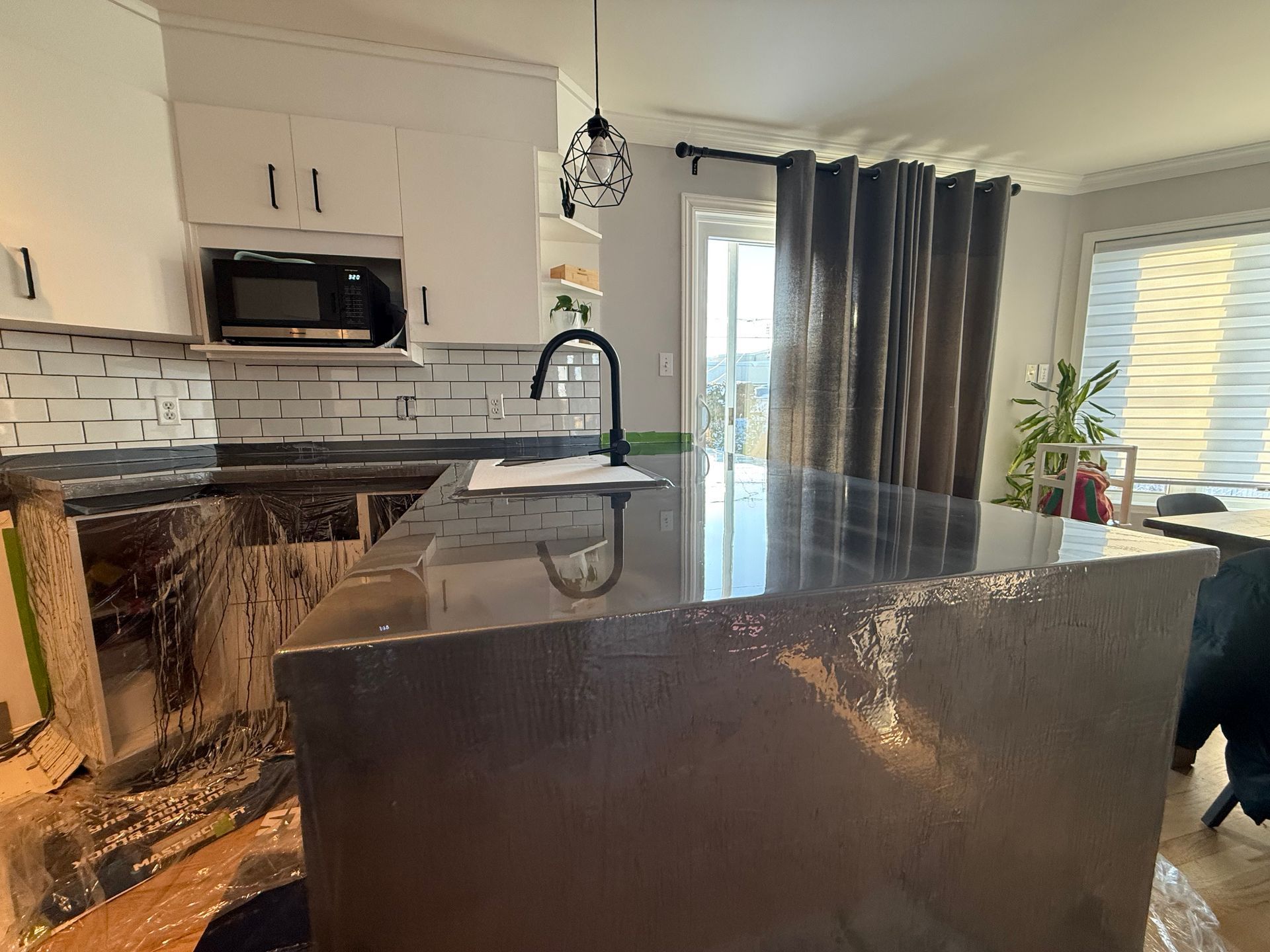 Cuisine avec comptoir d'îlot foncé, armoires, micro-ondes et une fenêtre avec rideaux.