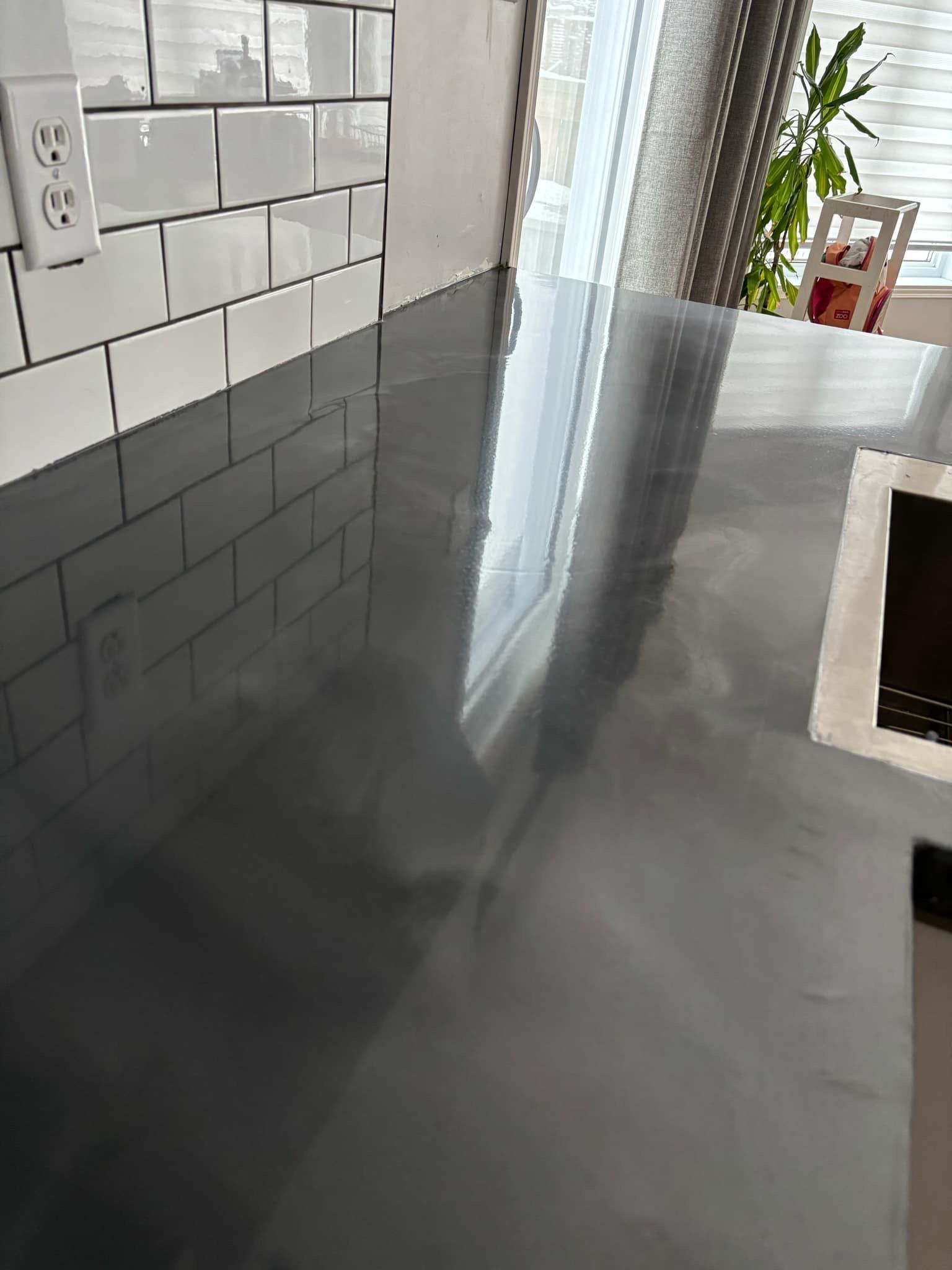 Le comptoir gris reflète la lumière, à côté d'un dosseret en carreaux de métro blancs et d'une fenêtre.