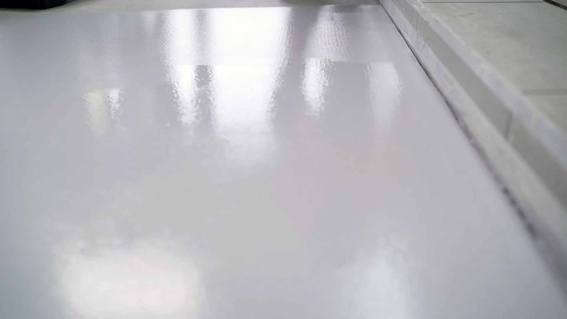 Sol blanc et brillant réfléchissant la lumière, près d'un bord de couleur claire, peut-être l'intérieur d'une pièce.