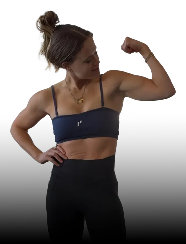 A smiling person wearing a beige baseball cap, black sports bra, and blue biker shorts with hands on their hips.