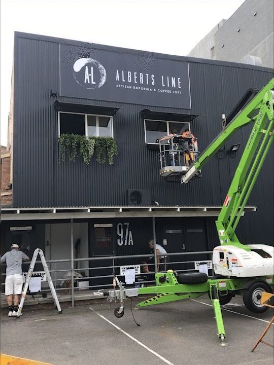 a green crane is being used to paint a sign on the side of a building