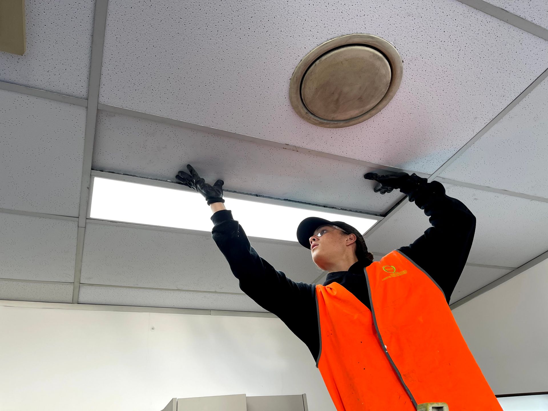 a man in an orange vest is working on a ceiling