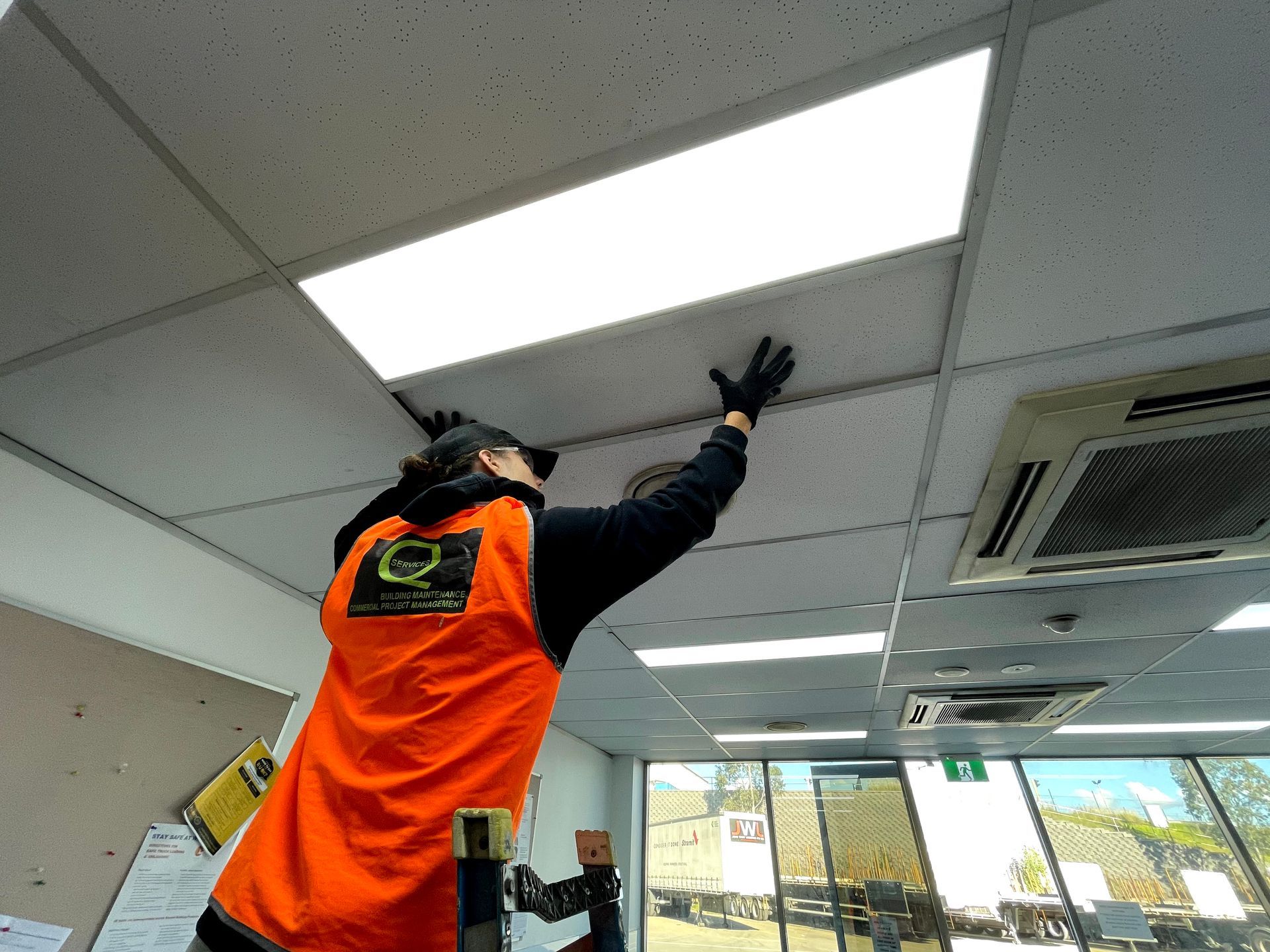 a man in an orange vest is working on a ceiling .