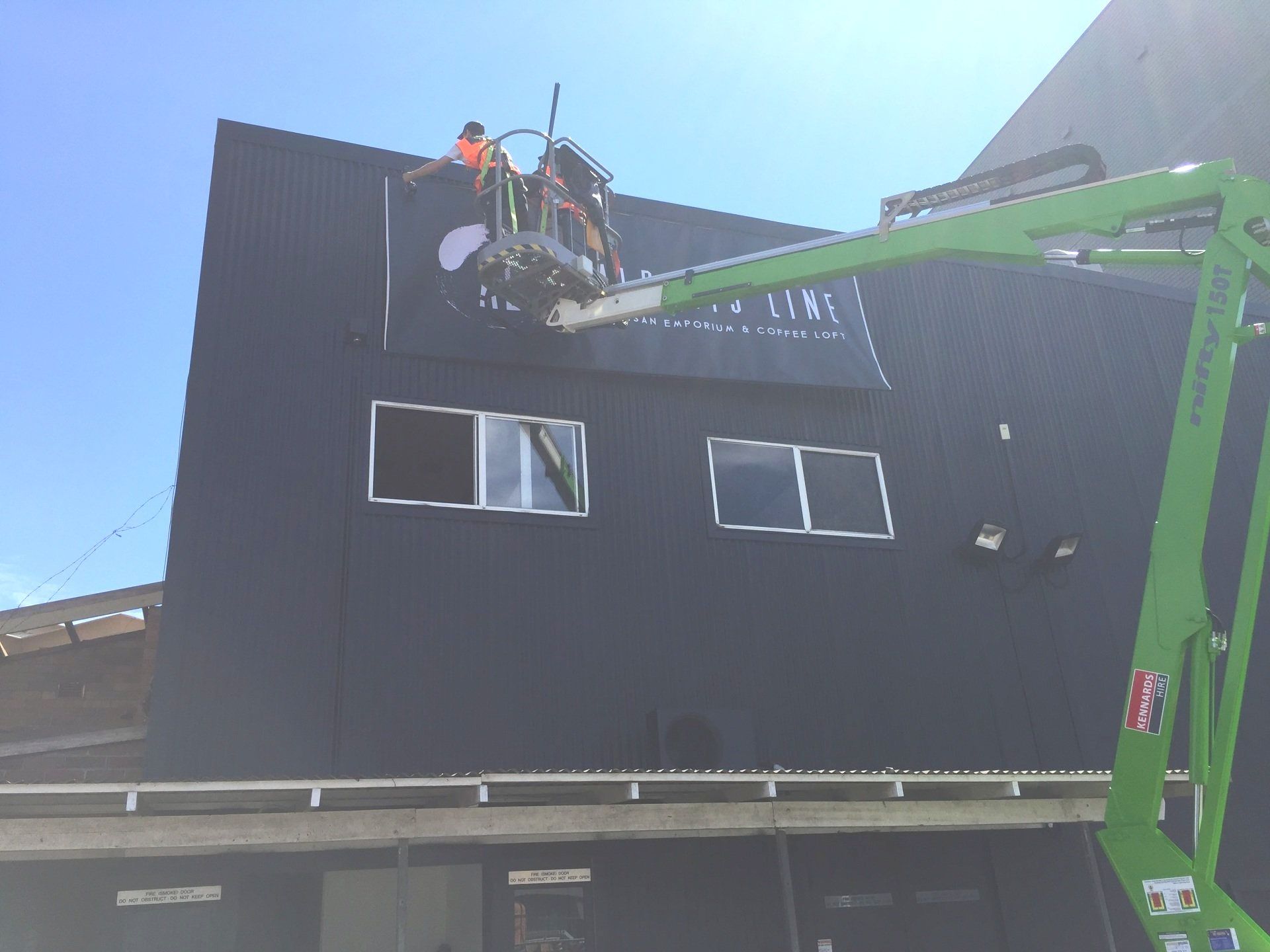 a green crane is lifting a sign on the side of a building .