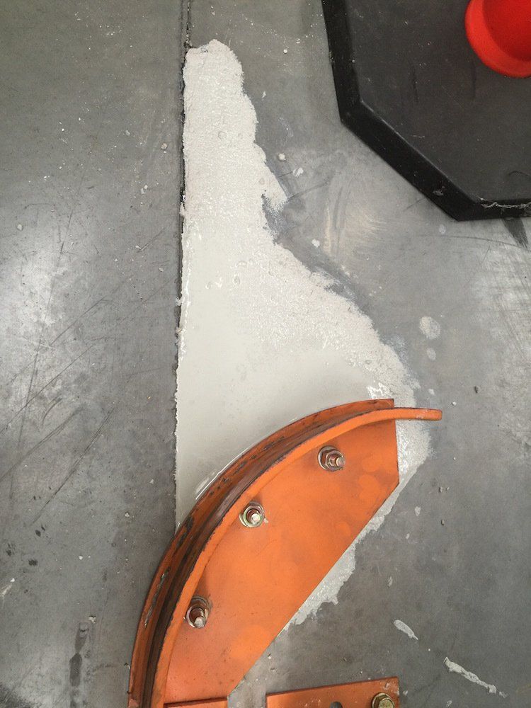 a piece of metal is sitting on a concrete floor next to a red cone .