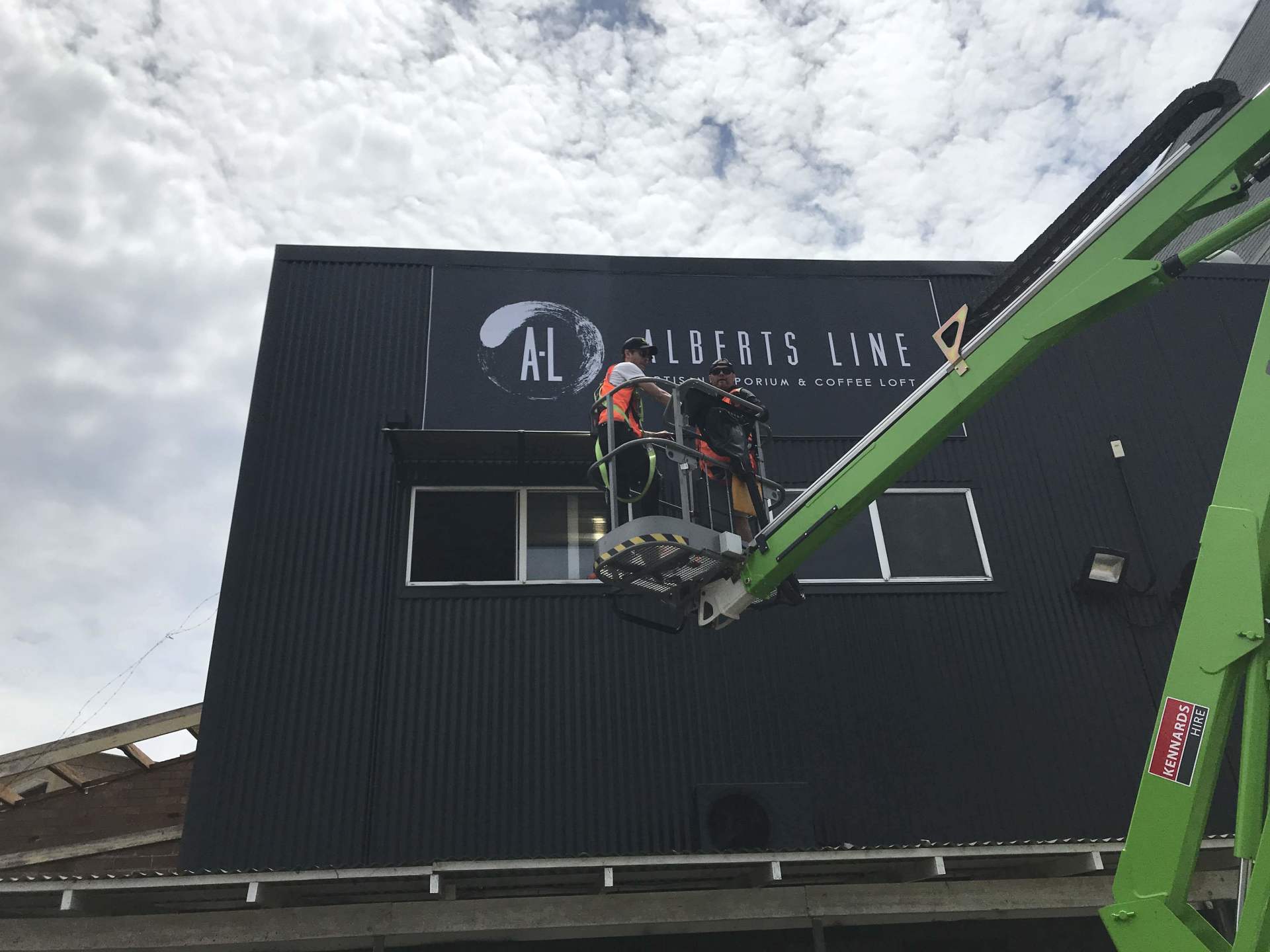 a green crane is lifting a sign on the side of a building .