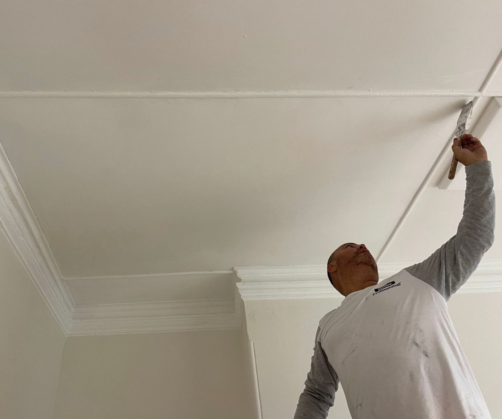 a man is painting the ceiling of a room with a brush .