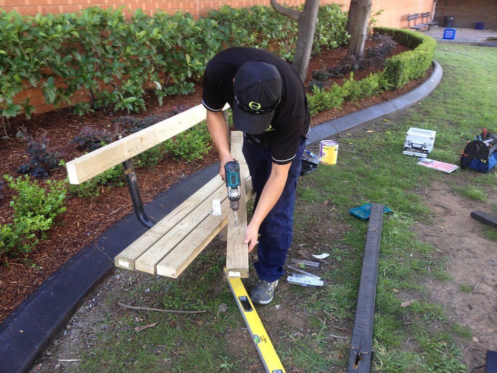 a man is working on a wooden bench with a drill .