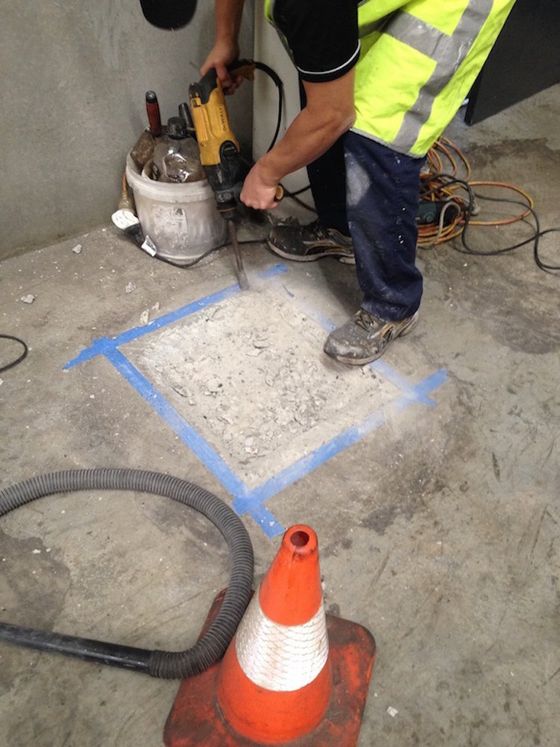 a man is using a drill on a concrete floor next to a traffic cone .