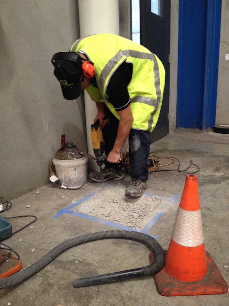 a man in a yellow vest is working on a concrete floor next to a traffic cone .
