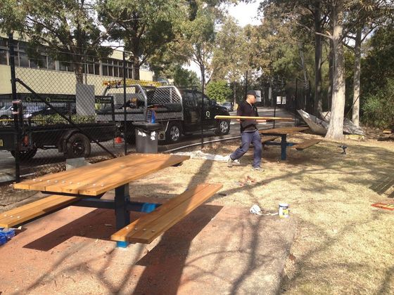 a man is painting a wooden picnic table in a park
