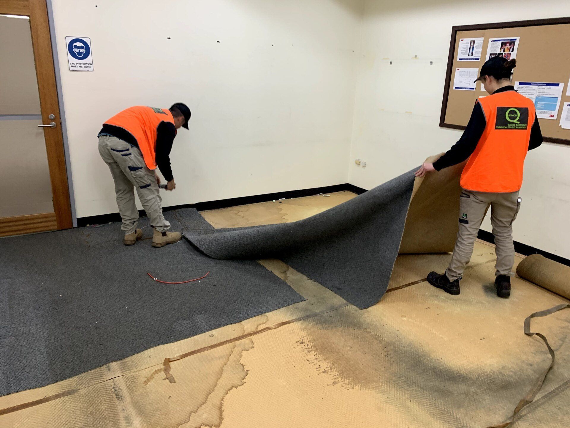 two men are laying carpet on the floor in a room .