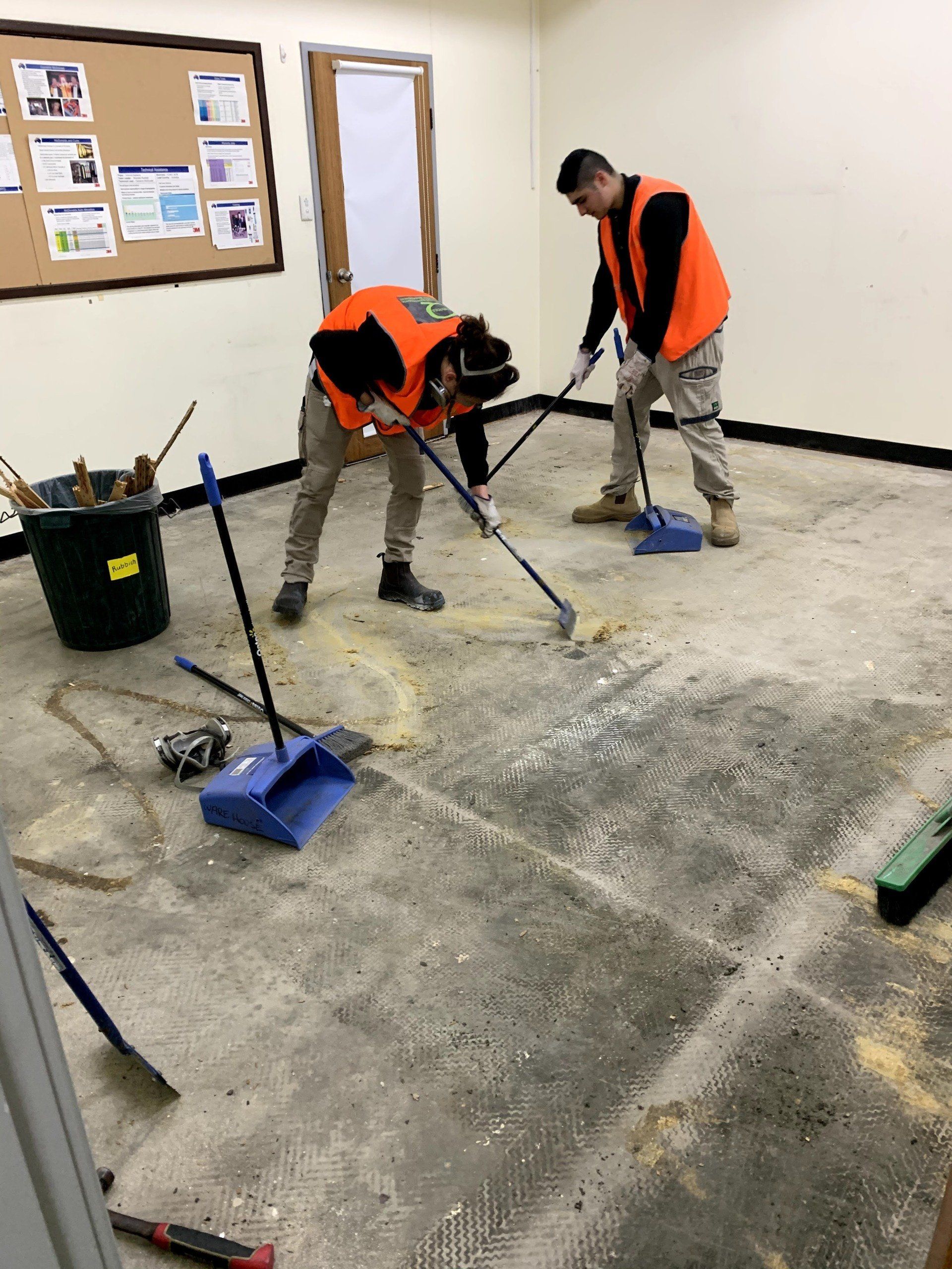 two men are cleaning the floor of a room with brooms .