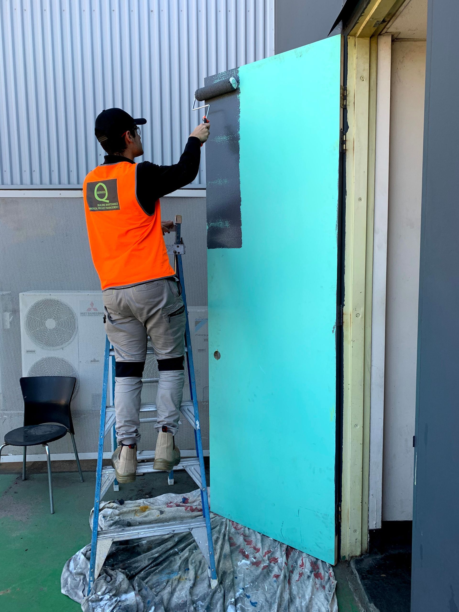 a man is standing on a ladder painting a door with a roller .