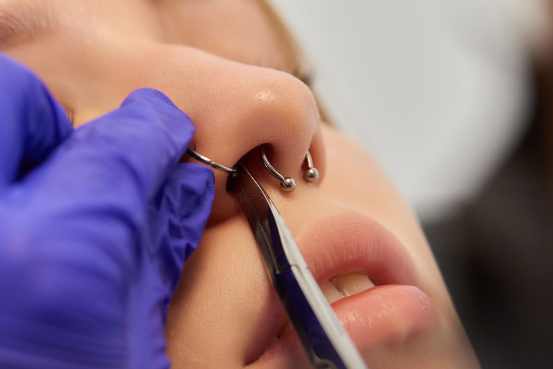 A person getting a nose piercing. A gloved hand uses pliers to insert jewelry into the nostril.