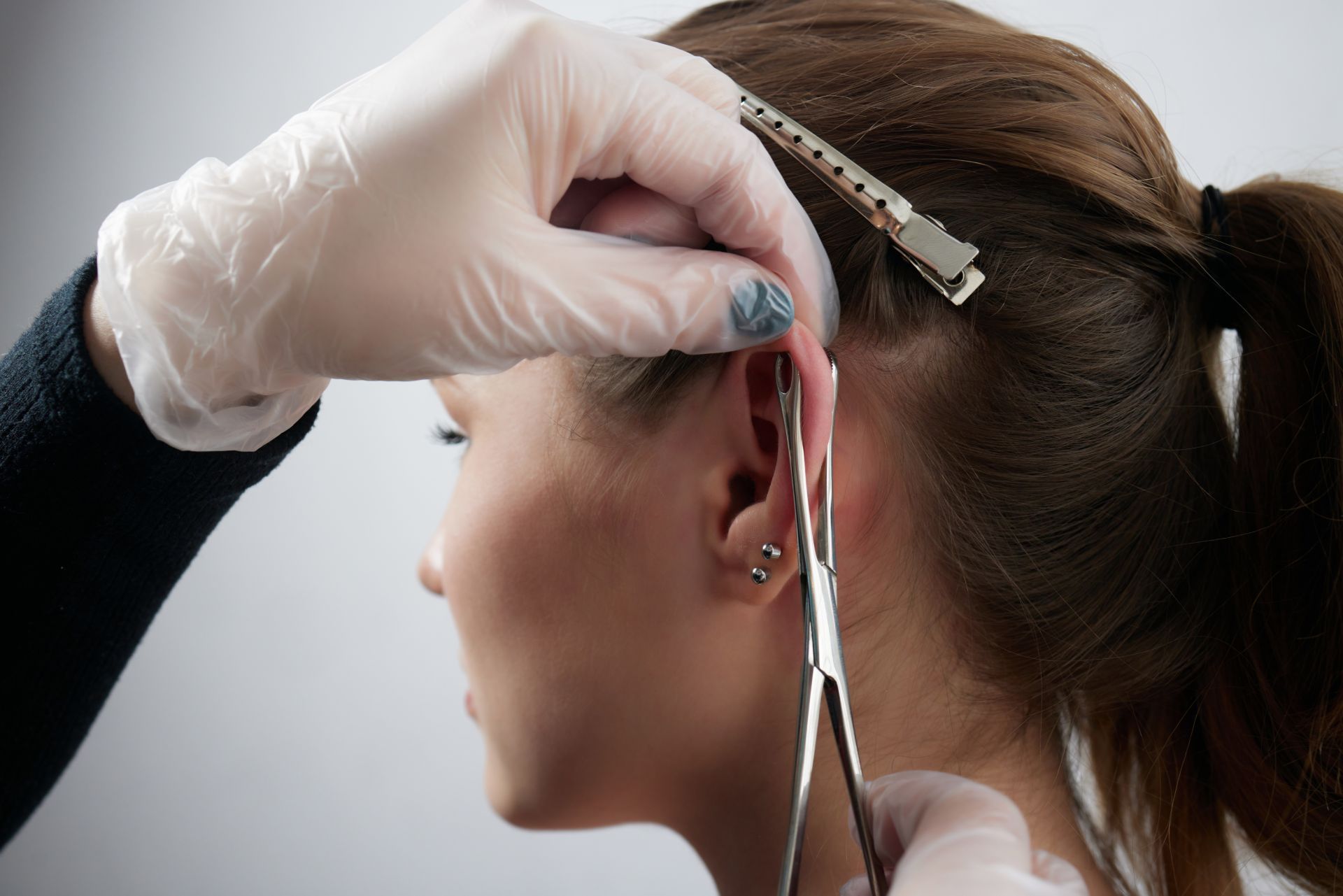 A person's ear being pierced with sterile tools by a person wearing gloves.